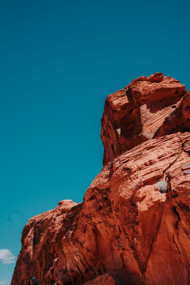 A red sandstone rock formation rising into the right side of the frame against a cloudless deep blue sky, with pale white patches and horizontal layering across its upper faces