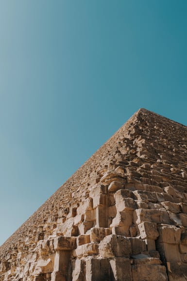 Low-angle view of a weathered stone pyramid against a clear blue sky.